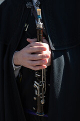 Un hombre con capa castellana negra sostiene entre sus manos una dulzaina o flauta dulce.