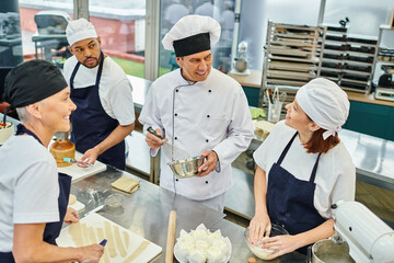 good looking jolly chief cook in white hat surrounded by his multiracial chefs, confectionery