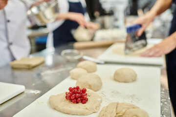 focused view of undercooked biscuit with red currant on table next to chefs and chief cook