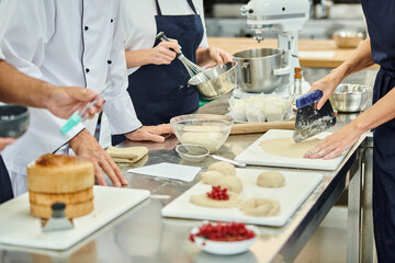 cropped view of hard working chefs and chief cook working with dough on kitchen, confectionery - obrazy, fototapety, plakaty