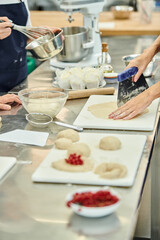 cropped view of team of chefs in blue aprons working together with dough on kitchen, confectionery