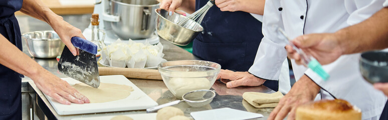 cropped view of hard working chefs in aprons working with dough on kitchen, confectionery, banner