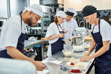 handsome mature chief cook in white hat talking to his hard working multiracial chefs on kitchen