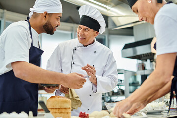Fototapeta na wymiar cheerful mature chief cook in white hat explaining information joyfully to his multiracial chefs