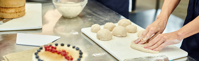 cropped view of mature chef working hard on dough next to her young colleague, confectionery, banner