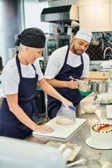 focus on young african american chef in toque whisking next to his blurred jolly mature colleague