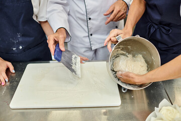 cropped view of mature chief cook showing his female chefs how to work with dough, confectionary