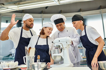 jolly multicultural chefs watching their chief cook showing them how to use mixer, confectionery