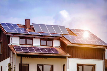 Fototapeta premium Solar Panels on Roof of Alpine House with White Facade with Sun Reflection. Photovoltaic Panels on Roof House.