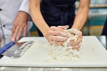 cropped view of mature female chef working with dough while chief cook helping her, confectionary