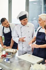 joyful mature chief cook smiling at his interracial chefs while they baking together, confectionary