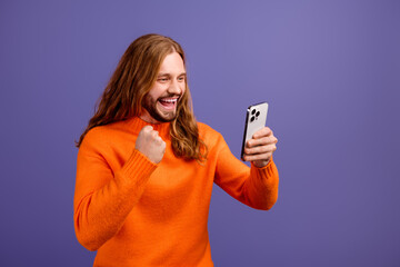 Portrait of young funny blond hair hipster addicted winner gamer cant stop betting using smartphone isolated on violet color background