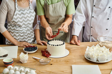 cropped view of mature woman decorating cake with berries next to chef and her young friend