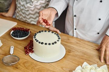 cropped view of mature chef decorating delicious cake with red currant next to his female student