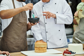 cropped view of young african american man brushing cake with syrup next to chef and his friends