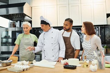 handsome mature chef talking to his multicultural students about how to cook, confectionary