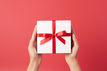 female hands of a white woman hold a white box decorated with a red bow on a red background. concept for Valentine's Day, March 8, love, new year, birthday.