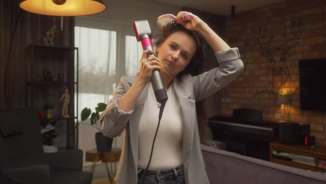 A woman dries her hair and makes a basal volume with a hairdryer and comb. A professional video tutorial on styling long, unruly curly hair with a hairdryer and brush at home.