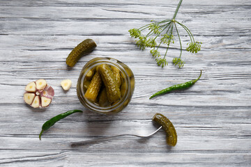 Canned cucumbers in an open jar, gherkin on a fork, garlic and hot pepper, top view.