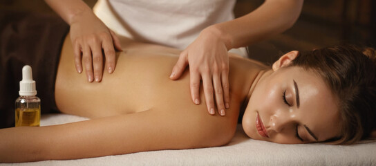 girl is lying on the massage table and enjoying an essential oil massage. The masseur's hand gently presses the girl's waist. The essential oil flows on the girl's skin - obrazy, fototapety, plakaty