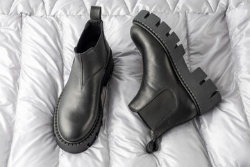 Trendy fashionable black leather short  women pair chelsea boots  with rough sole on silver metal color down jacket background.