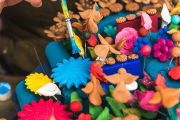 Detail of the hand of an artisan painting a tree of life made of clay in different colors with a brush.