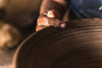 Detail of the hands of an artisan making a clay pot with his tools.