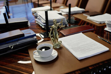Empty workplace in conference room with documents and statue of lady justice on large wooden table