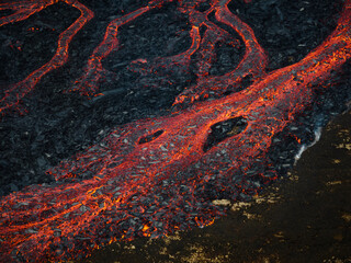 Unique view of molten lava flow burning and slowly moving down rugged volcanic rocks terrain, aerial close up shot. Volcano eruption and natural disaster concepts.