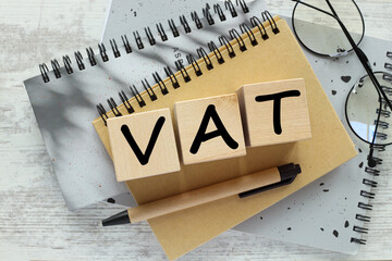 VAT concept in 2024. Wooden letter VAT and number 2024 on a wooden block on a gray notepad. Value added tax.