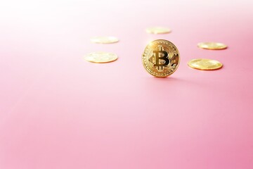 Close up golden bitcoin coin on light pink background. Cryptocurrency symbol. The shiny bitcoin gold coin stands out in front of other coins with copy space.
