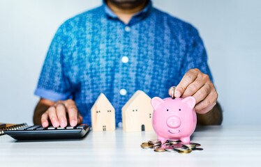 Close-up man holding a pink pig piggy bank and collecting coins in a piggy bank. Concept of men collects money for a home and car payment during COVID or coronavirus outbreak. Blurred white background