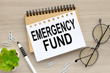 EMERGENCY FUND : Concept of setting money saving goal for rainy day. text on an open notepad. on a...