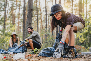 Active young woman with hat cleaning forest in plastic bag, ecology helping environment garbage...