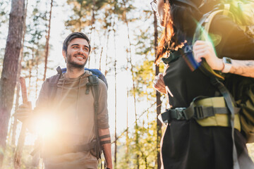 Loving couple going for a camping trip with backpacks walking through forest looking on each other. Away from everything, escaping from urban life to wild woods