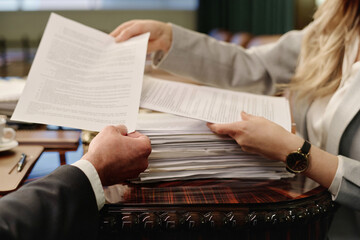 Hands of unrecognizable caucasian male and female lawyers passing documents to each other
