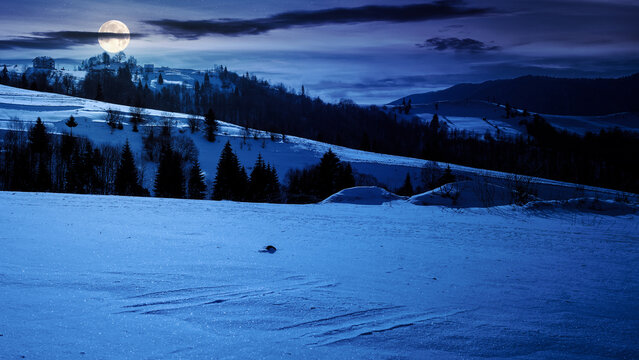 mountainous winter landscape at night. snow covered hills and meadow in full moon light