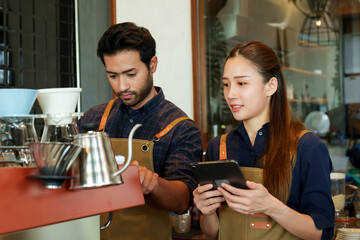 The Coffee shop owner is preparing to make coffee. According to orders that customers order through online applications on tablets. beautiful asian woman and husband Check coffee orders and prepare..