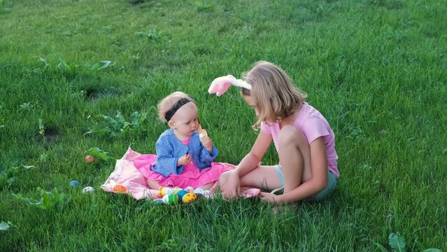 Adorable baby with little girl playing on with painted eggs on a grass. Easter hunt concept