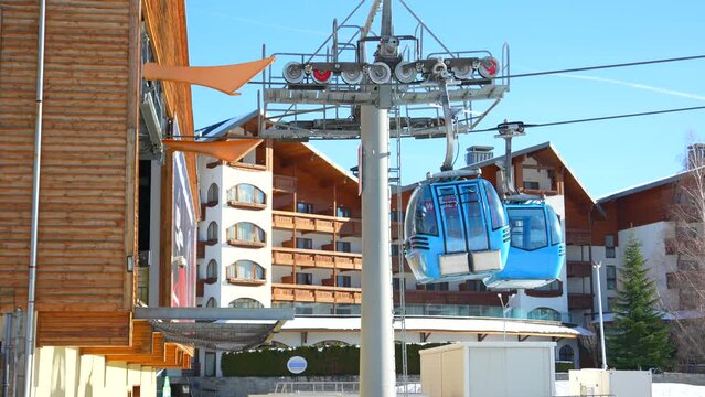 Cable cars are moving over the cableway next to gondola station on a sunny winter day.
