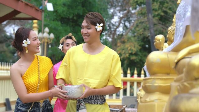 A couple wearing traditional Thai clothing smiles at each other, expressing their joy at the ceremony of bathing a Buddha image during the Thai Songkran festival.