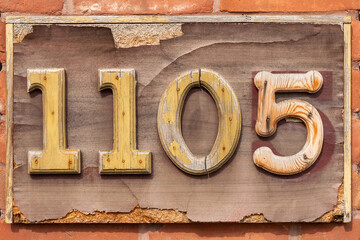 Street number 1105, eleven zero five, on house wall, old sign close-up on brick wall background.