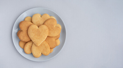 Plate of delicious heart-shaped cookies on light grey background. Minimalist composition for Valentine's Day. Copy space, top view.