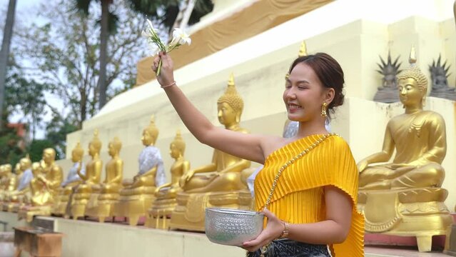 A beautiful girl wearing a Thai traditional dress is happy. The ceremony of bathing Buddha images during the Thai Songkran festival