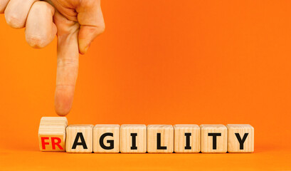 Fragility or agility symbol. Concept words Fragility and Agility on wooden cubes. Beautiful orange table orange background. Businessman hand. Business fragility and agility concept. Copy space.