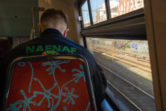 Paris, France - February 21, 2023: Young (unrecognizable; back view) man wearing Naf Naf bomber jacket travels from suburb to city by train line RER A. Naf Naf is popular fashion brand founded in 1973