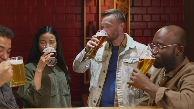 Medium footage of group of diverse friends hanging out in bar celebrating and cheering with beer in evening