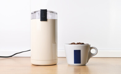 White electric coffee grinder with a cup of coffee on a white background.