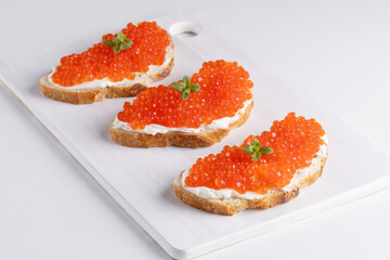 Three sandwiches with red caviar on a cutting board. A delicious appetizer of trout caviar on a slice of bread with cream cheese. Salted salmon caviar for fish delicacy concept