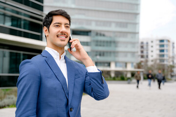 A young Hispanic businessman in a stylish blue suit speaks on the phone, with a bustling city life backdrop, embodying the concept of global connectivity and on-the-go business management.